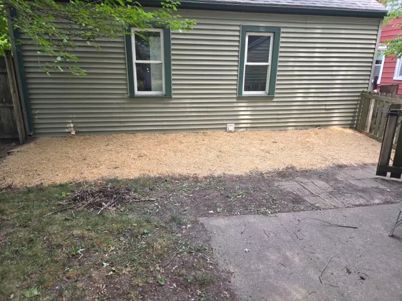 Long low berm covered with tan material beside a sided house, next to grass and a paved path