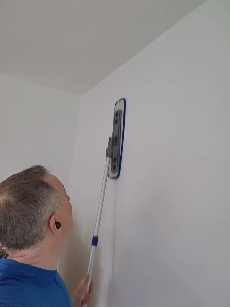 Technician cleaning a painted wall with a flat pad on an extension handle